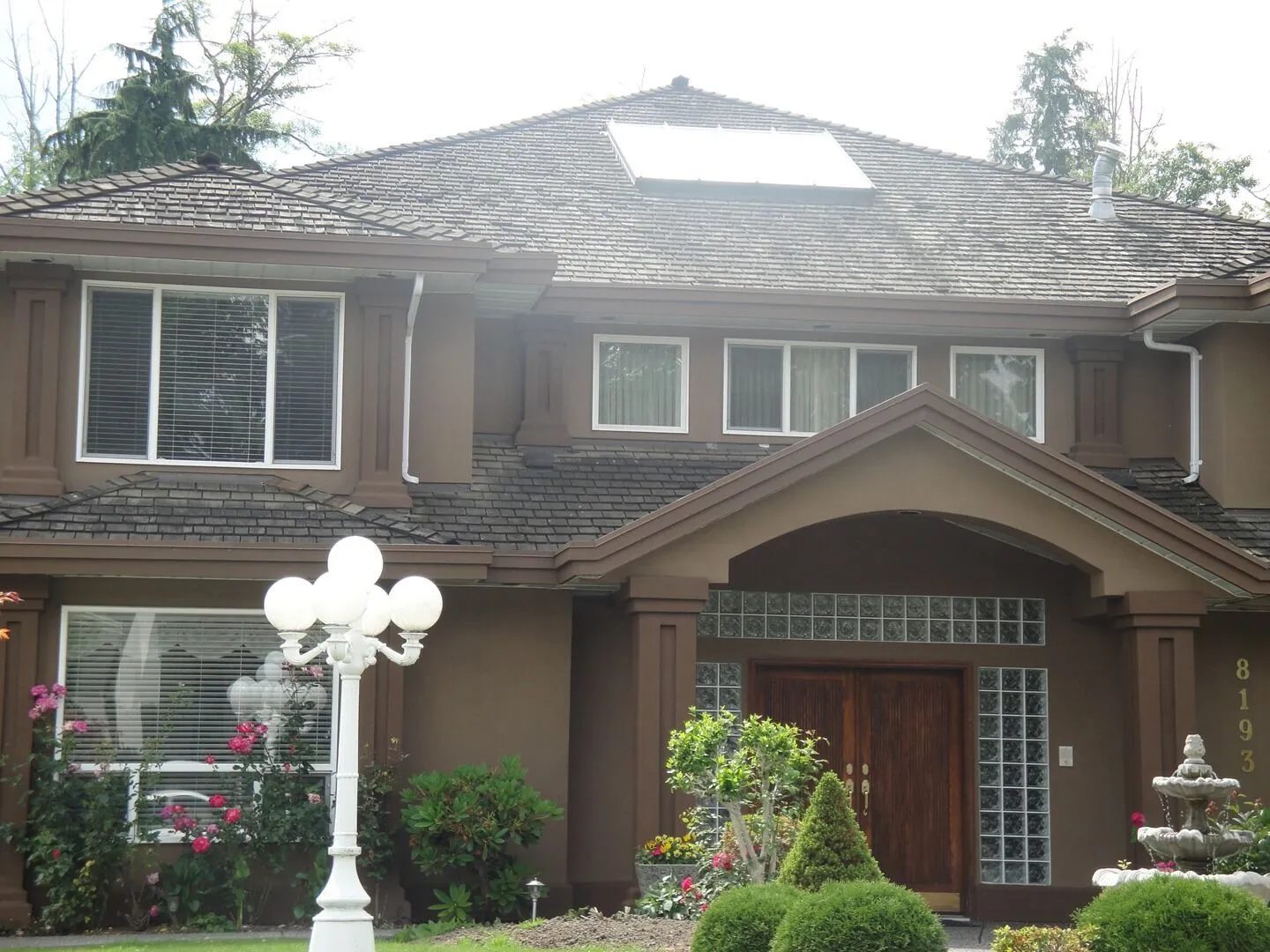 Large stucco home painted deep brown with wood double doors