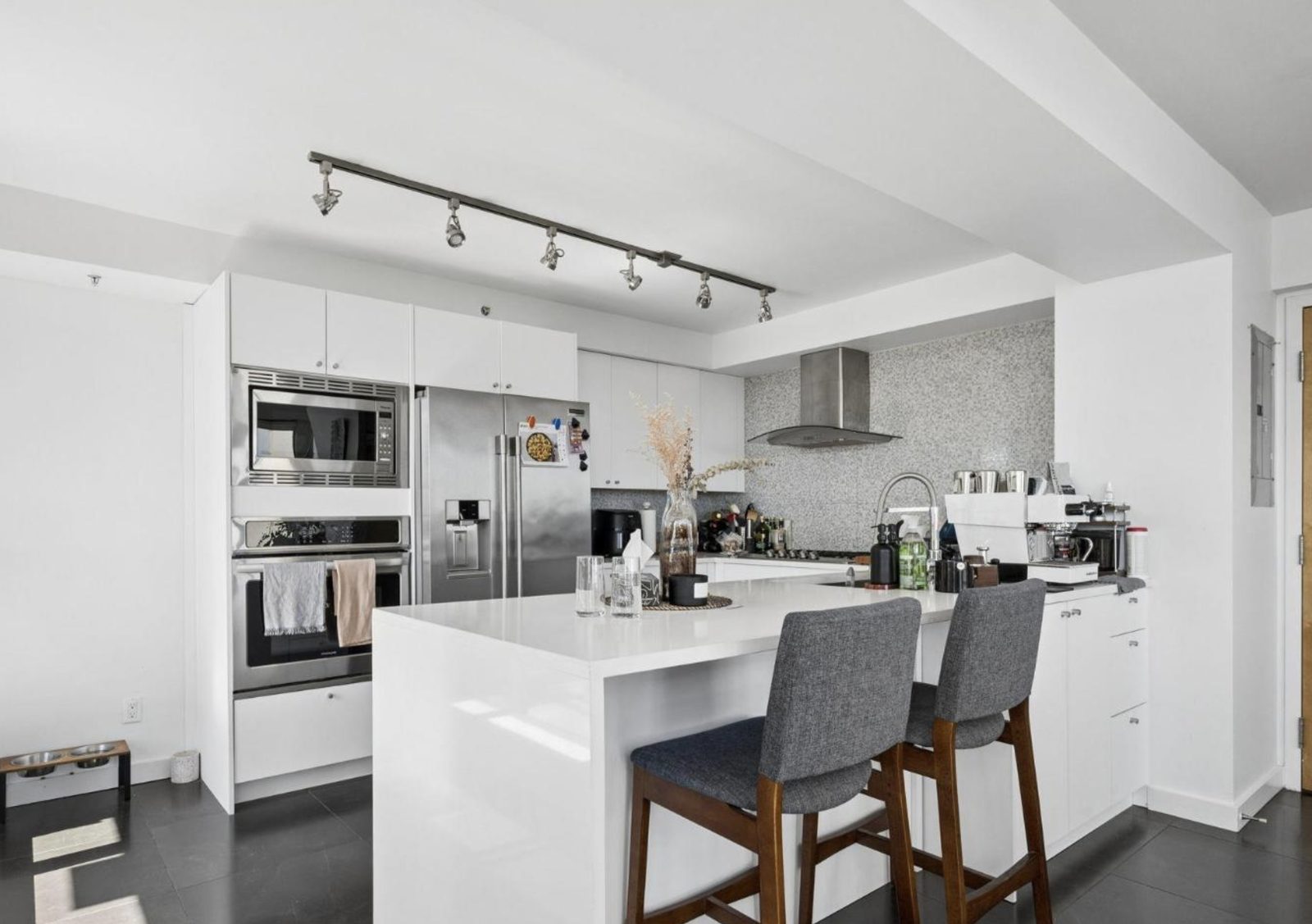 Bright white kitchen with an island, track lighting and stainless appliances